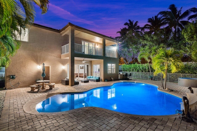 pool at dusk featuring fence, a patio area, outdoor lounge area, and a ceiling fan