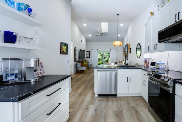 kitchen featuring stainless steel appliances, a peninsula, light wood-type flooring, open floor plan, and dark countertops