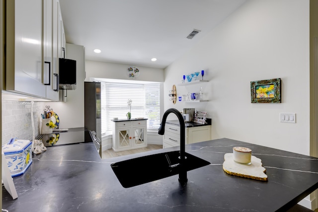 kitchen featuring dark countertops, visible vents, white cabinetry, and a sink