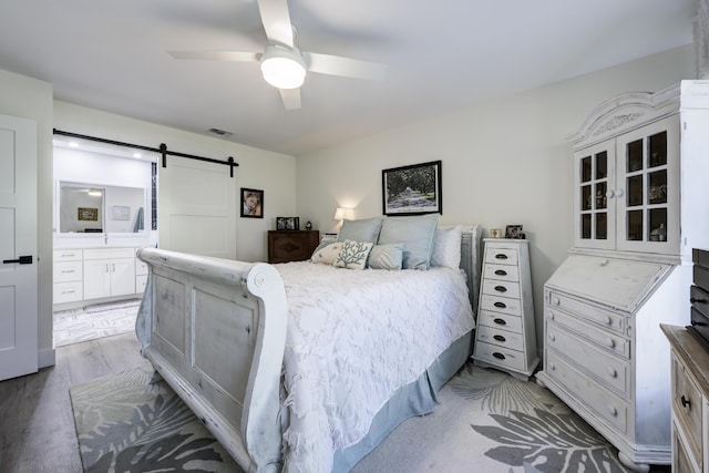 bedroom featuring a barn door, visible vents, light wood-style floors, ensuite bath, and ceiling fan