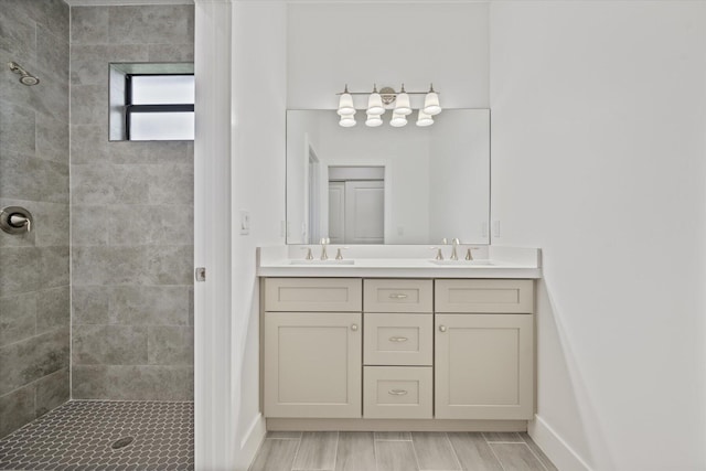 bathroom with double vanity, baseboards, tiled shower, and a sink