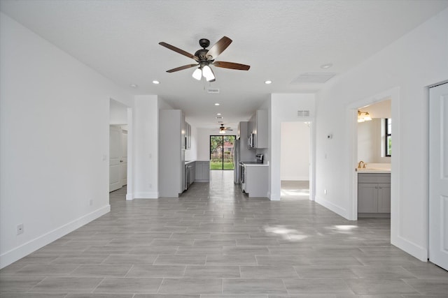 unfurnished living room with ceiling fan, a sink, recessed lighting, baseboards, and visible vents