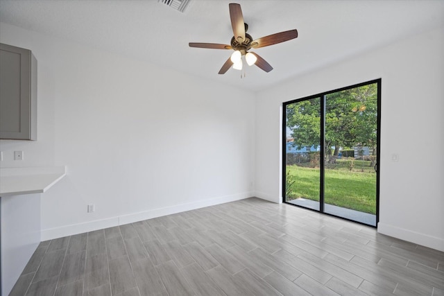 empty room with baseboards, a ceiling fan, wood finished floors, and visible vents