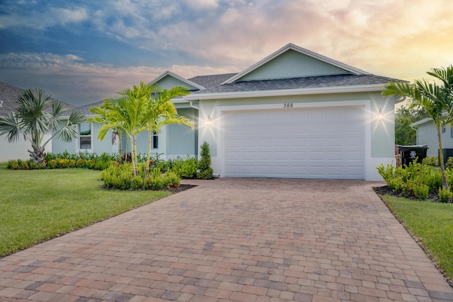 single story home featuring driveway, an attached garage, a lawn, roof with shingles, and stucco siding