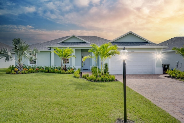 view of front of property with decorative driveway, a garage, a front yard, roof with shingles, and stucco siding