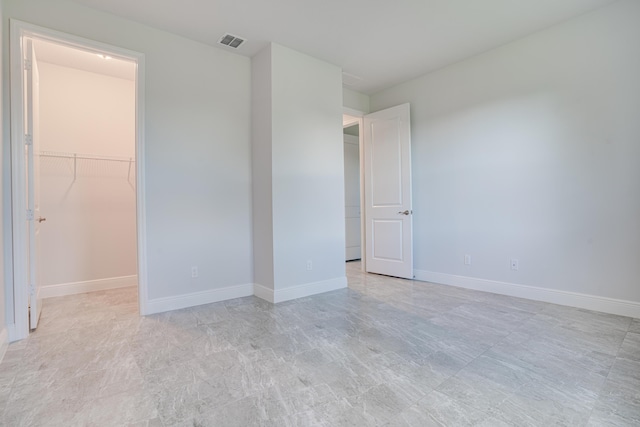 unfurnished bedroom with baseboards, a closet, visible vents, and a walk in closet