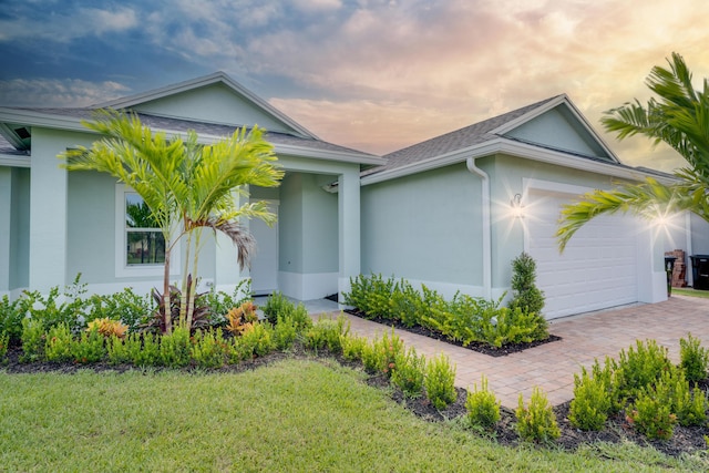 exterior space with decorative driveway, a garage, a front lawn, roof with shingles, and stucco siding