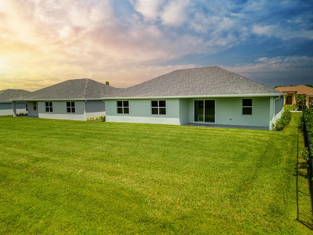 rear view of house with a shingled roof, stucco siding, and a yard