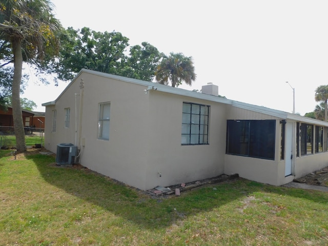 view of property exterior featuring stucco siding, a lawn, a chimney, and central AC unit