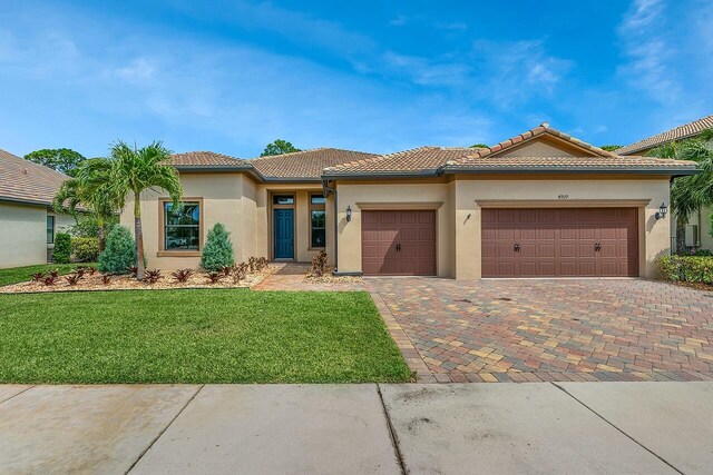 view of front facade with a front yard, an attached garage, a tile roof, stucco siding, and decorative driveway