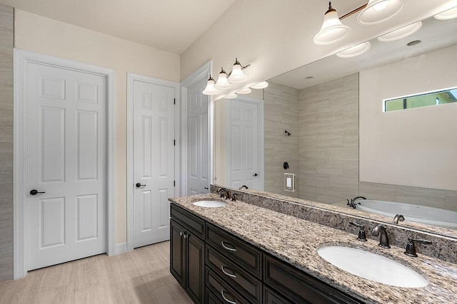 full bath with a tile shower, wood finished floors, double vanity, and a sink