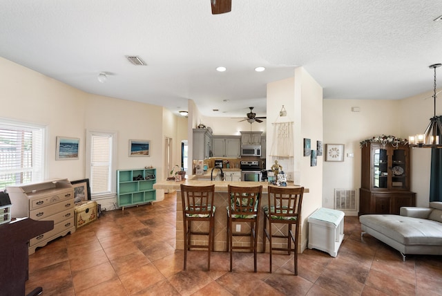 tiled dining space with ceiling fan with notable chandelier, visible vents, a sink, and recessed lighting