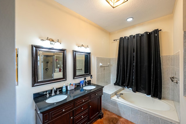 bathroom featuring a relaxing tiled tub, a sink, double vanity, and a textured ceiling
