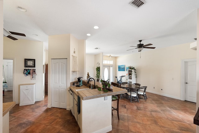 kitchen with a kitchen bar, ceiling fan, tile counters, and visible vents