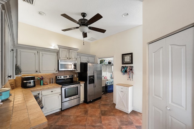 kitchen with stainless steel appliances, visible vents, tile countertops, tasteful backsplash, and ceiling fan