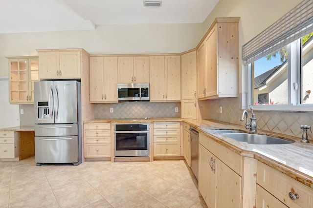 kitchen with light brown cabinetry, a center island, a sink, stainless steel appliances, and tasteful backsplash