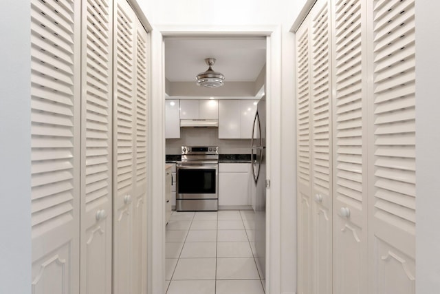 kitchen with electric range, under cabinet range hood, dark countertops, white cabinets, and light tile patterned floors