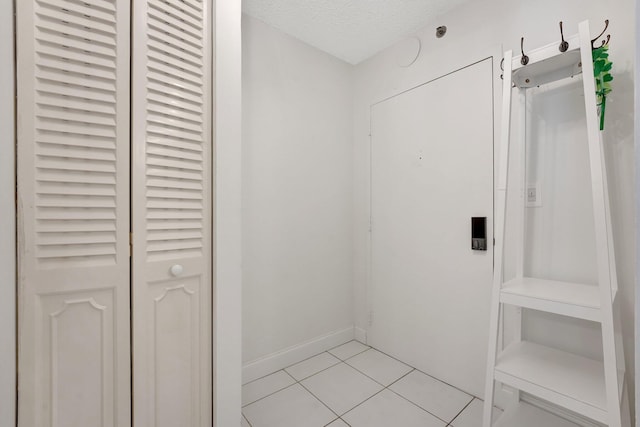 corridor featuring light tile patterned floors, a textured ceiling, and baseboards