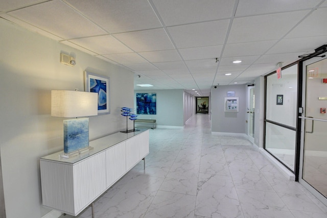 corridor with recessed lighting, a drop ceiling, marble finish floor, and baseboards