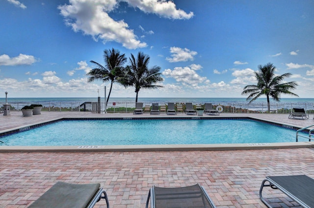 community pool featuring a water view, a patio, and fence