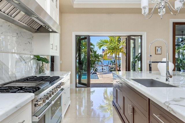 kitchen featuring a sink, extractor fan, an inviting chandelier, range with two ovens, and light stone countertops