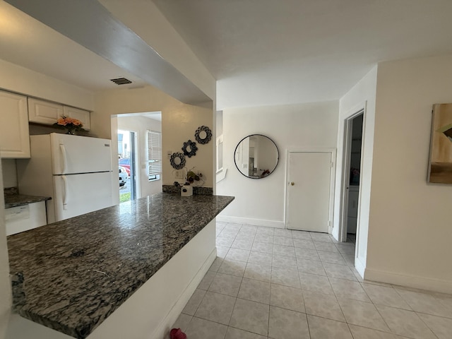 kitchen featuring dark stone countertops, light tile patterned floors, white cabinets, baseboards, and freestanding refrigerator