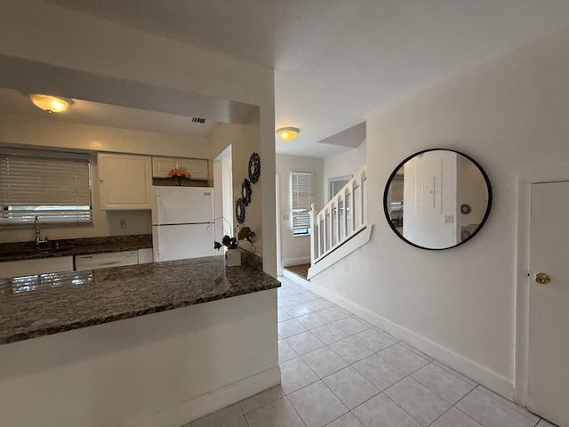 kitchen featuring dark stone counters, a sink, white appliances, light tile patterned floors, and baseboards