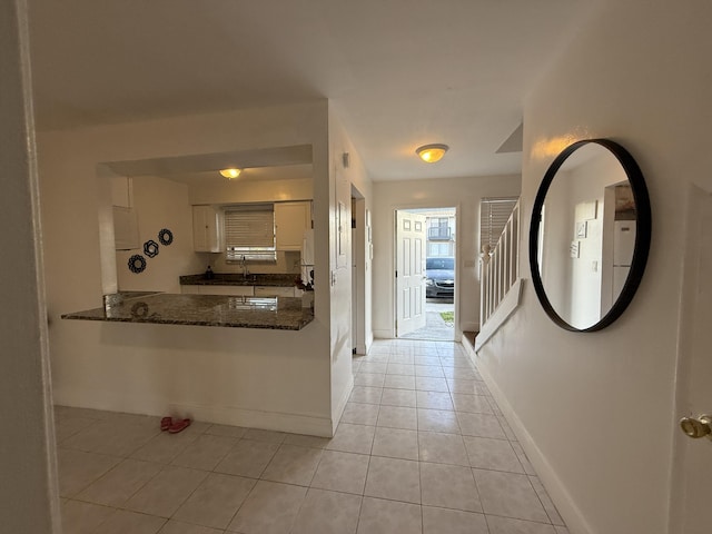 corridor featuring baseboards, light tile patterned flooring, and stairs