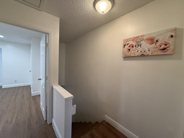 hall featuring an upstairs landing, baseboards, wood finished floors, and a textured ceiling