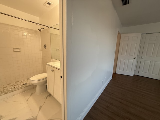 full bath with a tile shower, toilet, vanity, and visible vents