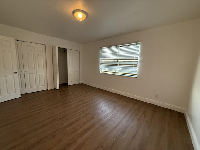 unfurnished bedroom with multiple closets, baseboards, and dark wood-style flooring