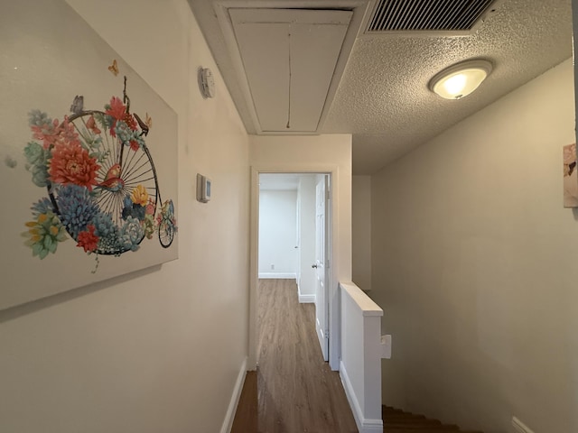 hall with attic access, dark wood finished floors, baseboards, visible vents, and an upstairs landing