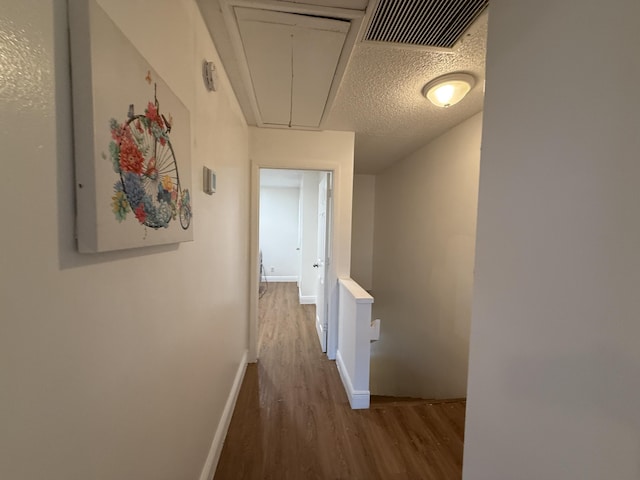 corridor with attic access, wood finished floors, visible vents, and baseboards