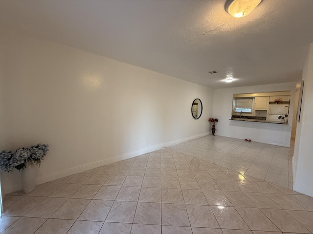 unfurnished living room with baseboards, a textured ceiling, visible vents, and light tile patterned floors