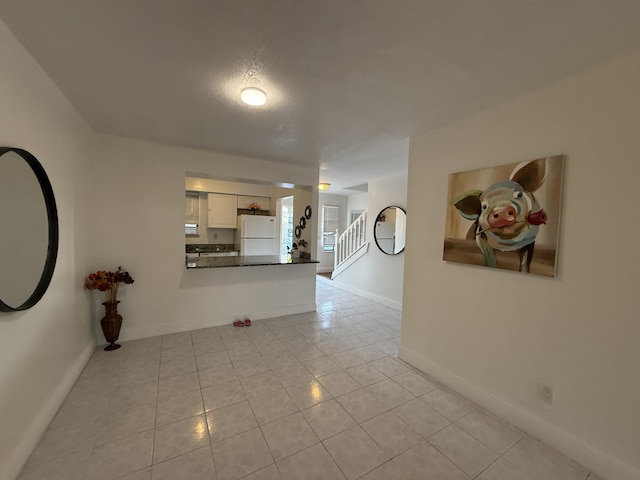 corridor featuring stairway, baseboards, and light tile patterned floors