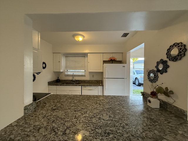 kitchen featuring dark stone countertops, a sink, white appliances, white cabinets, and visible vents