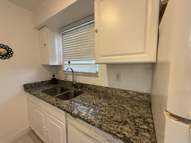 kitchen featuring white cabinets, light tile patterned floors, a sink, freestanding refrigerator, and dark stone counters