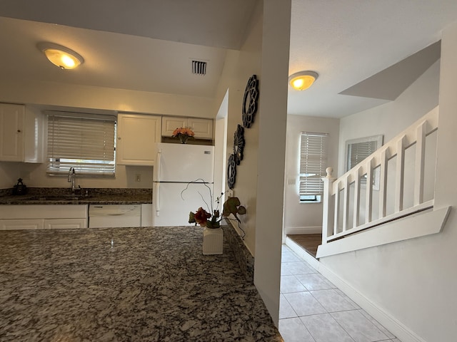 kitchen featuring visible vents, a sink, light tile patterned flooring, white appliances, and dark stone counters