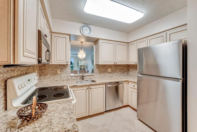 kitchen with tasteful backsplash, appliances with stainless steel finishes, a sink, cream cabinets, and light tile patterned floors