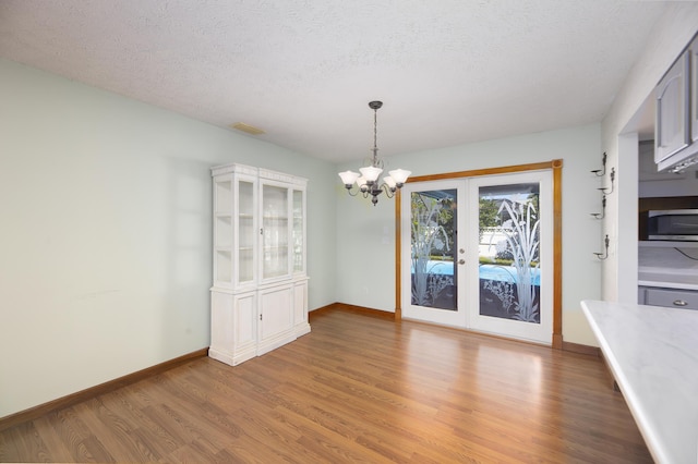 unfurnished dining area featuring baseboards, a chandelier, a textured ceiling, light wood-style floors, and visible vents