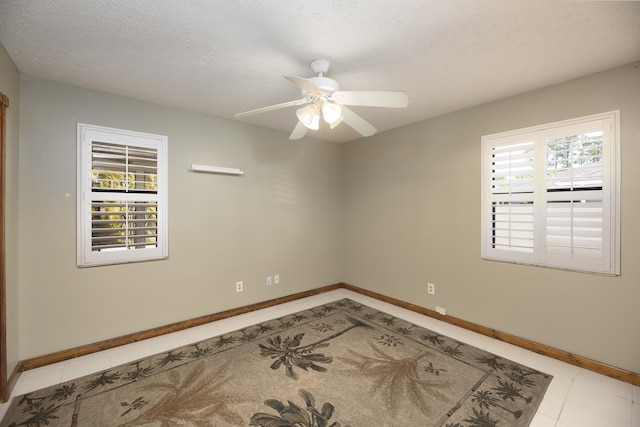 empty room featuring baseboards, ceiling fan, light tile patterned floors, and a textured ceiling