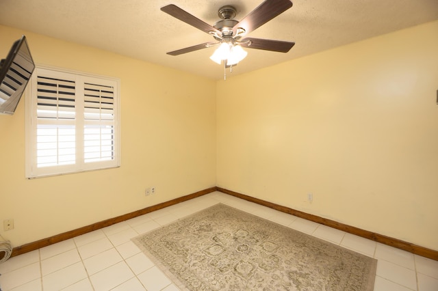 empty room featuring baseboards, a textured ceiling, a ceiling fan, and light tile patterned floors