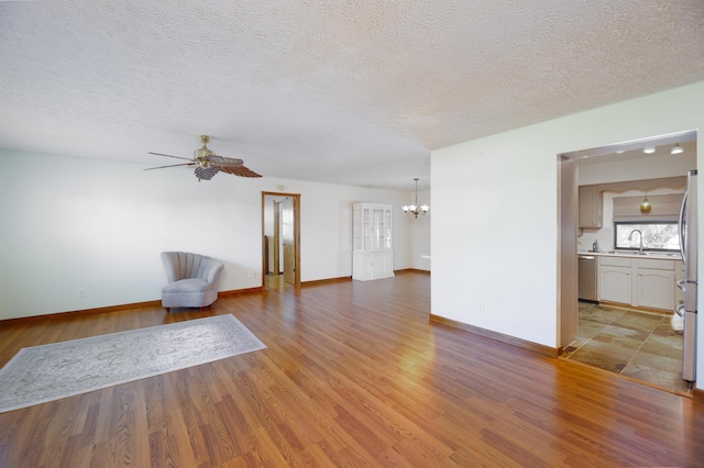 unfurnished living room featuring light wood-style flooring, a sink, ceiling fan with notable chandelier, and a textured ceiling