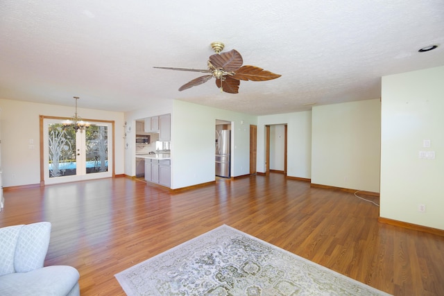 unfurnished living room with ceiling fan with notable chandelier, baseboards, and wood finished floors