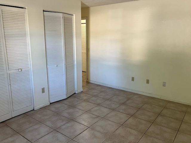 unfurnished bedroom featuring light tile patterned floors, baseboards, and multiple closets