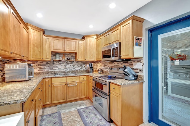 kitchen featuring light brown cabinetry, light stone counters, decorative backsplash, stainless steel appliances, and a sink