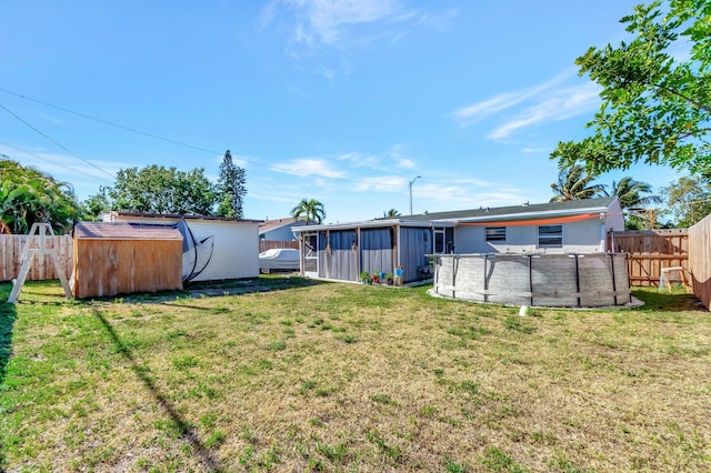 view of yard featuring a storage unit, an outbuilding, a swimming pool, a fenced backyard, and a sunroom