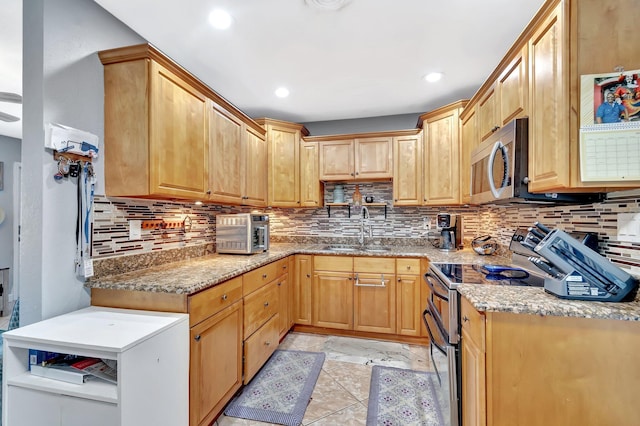 kitchen with a sink, light stone counters, tasteful backsplash, and appliances with stainless steel finishes