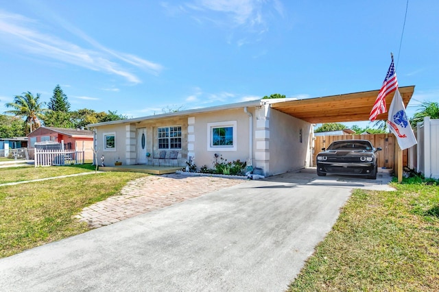 view of front facade featuring stucco siding, an attached carport, a front lawn, and fence
