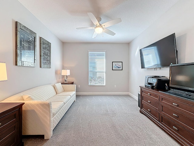 living area featuring light carpet, baseboards, a textured ceiling, and a ceiling fan